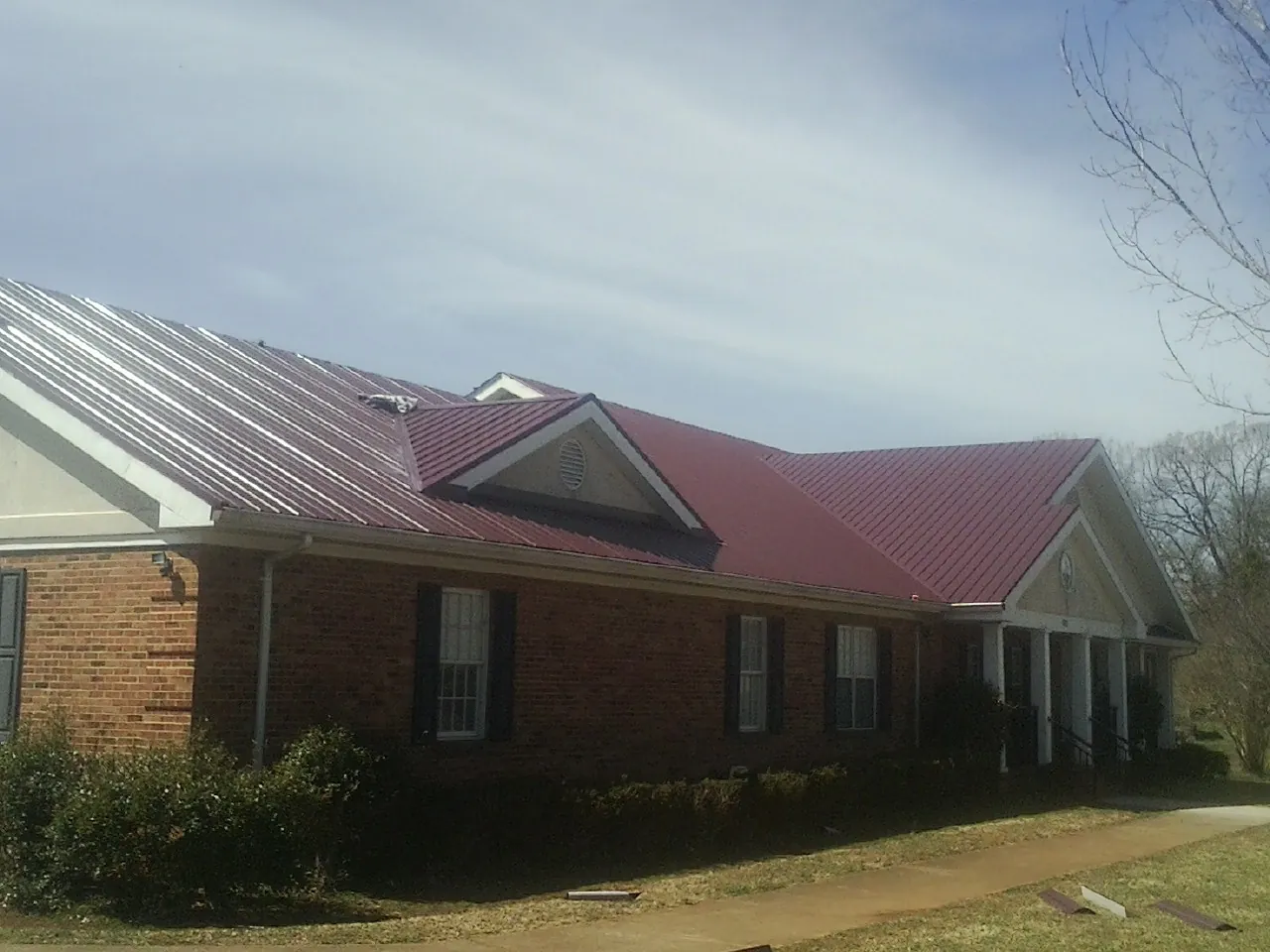 Red metal roof with gabled entries on a long brick building, from a Hail Damage Roof Repair job in Troy