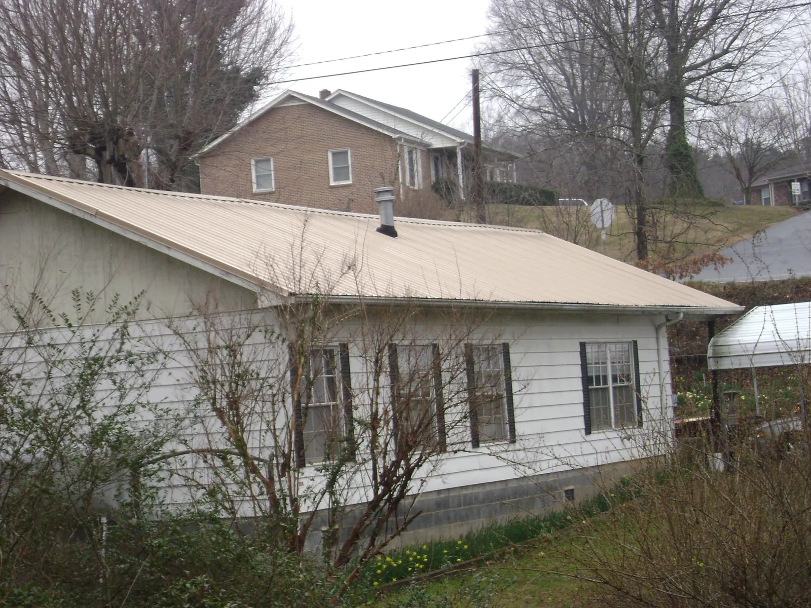 Tan metal roof on a white sided house set into a hillside — Commercial Roofing by Roofing Brothers in Troy